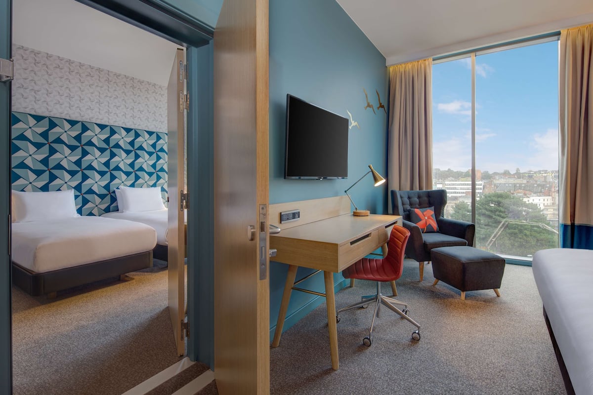 A hotel room with a bed, desk, chair, and a TV on the wall.