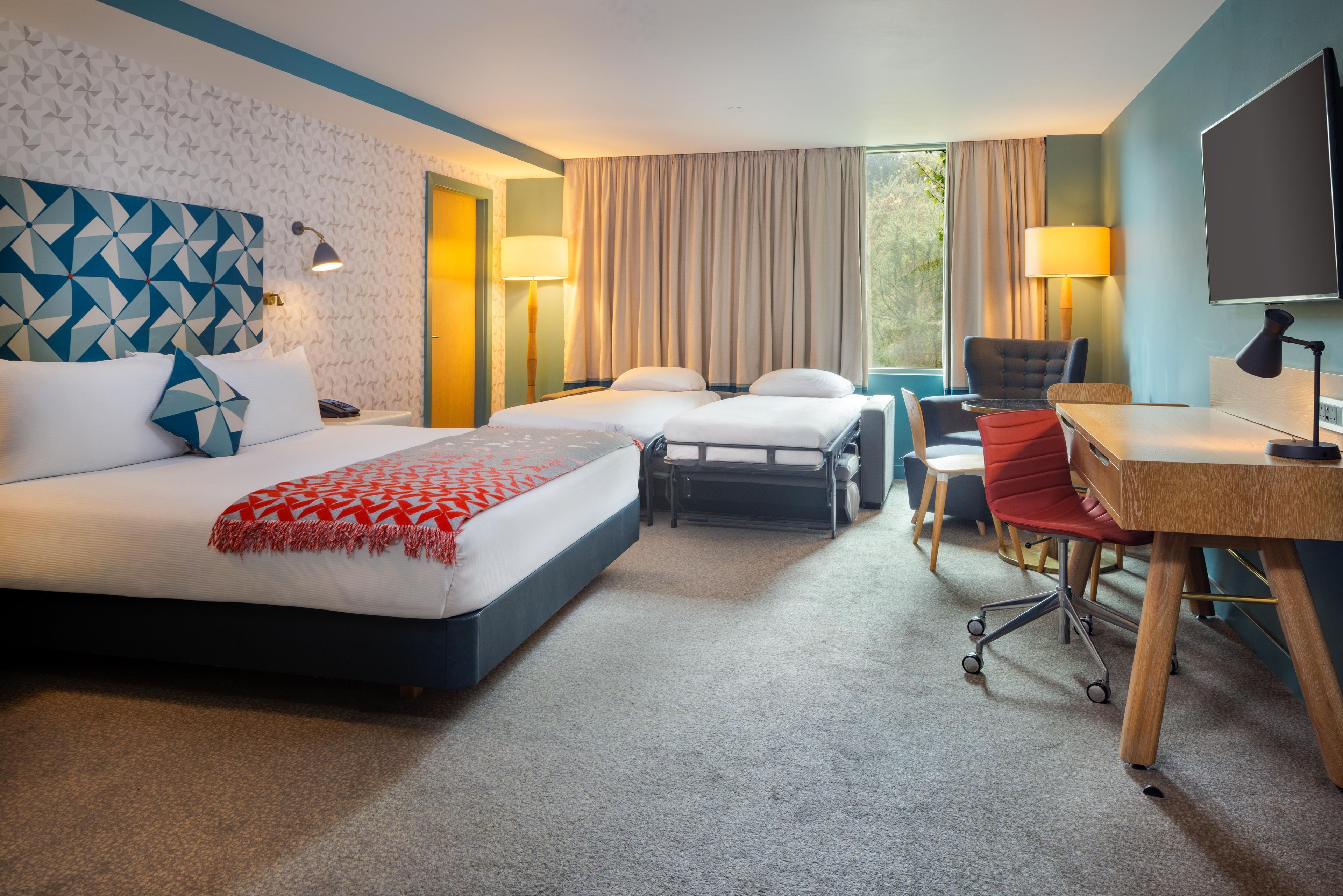 Ein Hotelzimmer mit Bett, Schreibtisch, Sessel und Fernseher.
