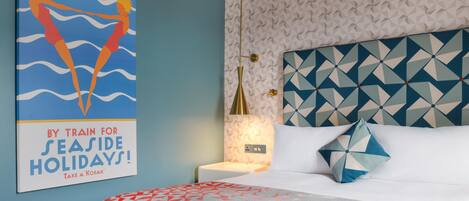 Een hotelkamer met een hoofdbord met geometrisch patroon, een bed met een decoratieve plaid, een nachtkastje met een lamp en een poster aan de muur.
