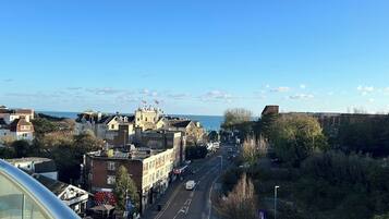 A city street with buildings, a clear sky, and a view of the sea.
