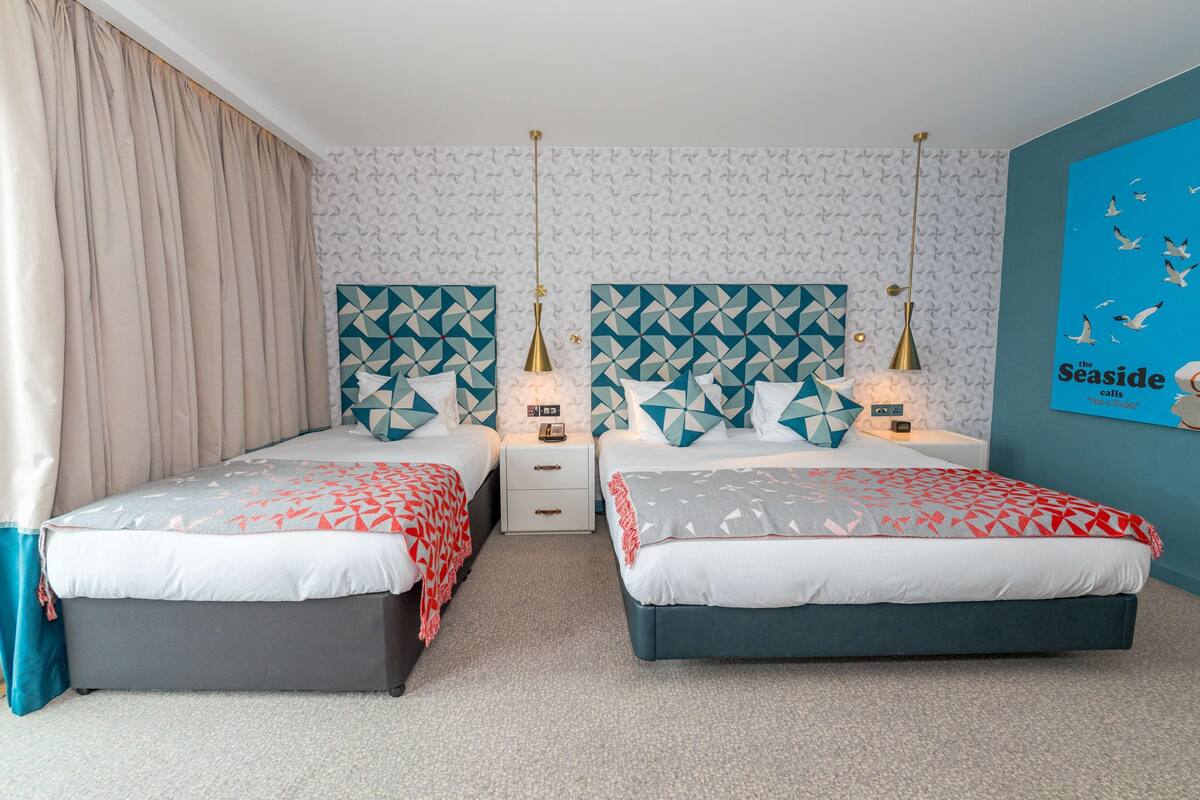 A double room with two beds, a nightstand, a lamp, and a poster on the wall.
