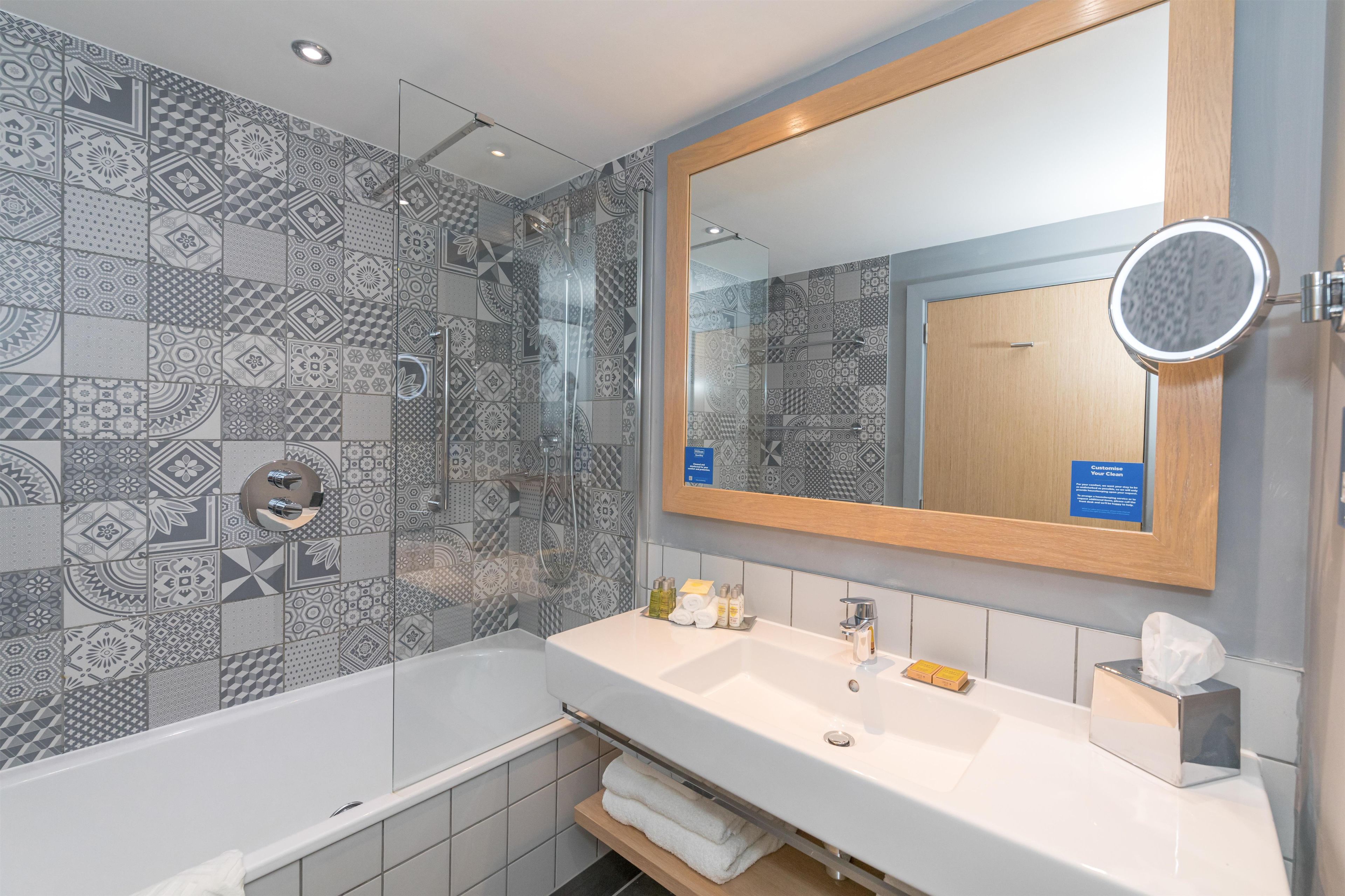 A modern bathroom with a shower, a large mirror, and a white sink.