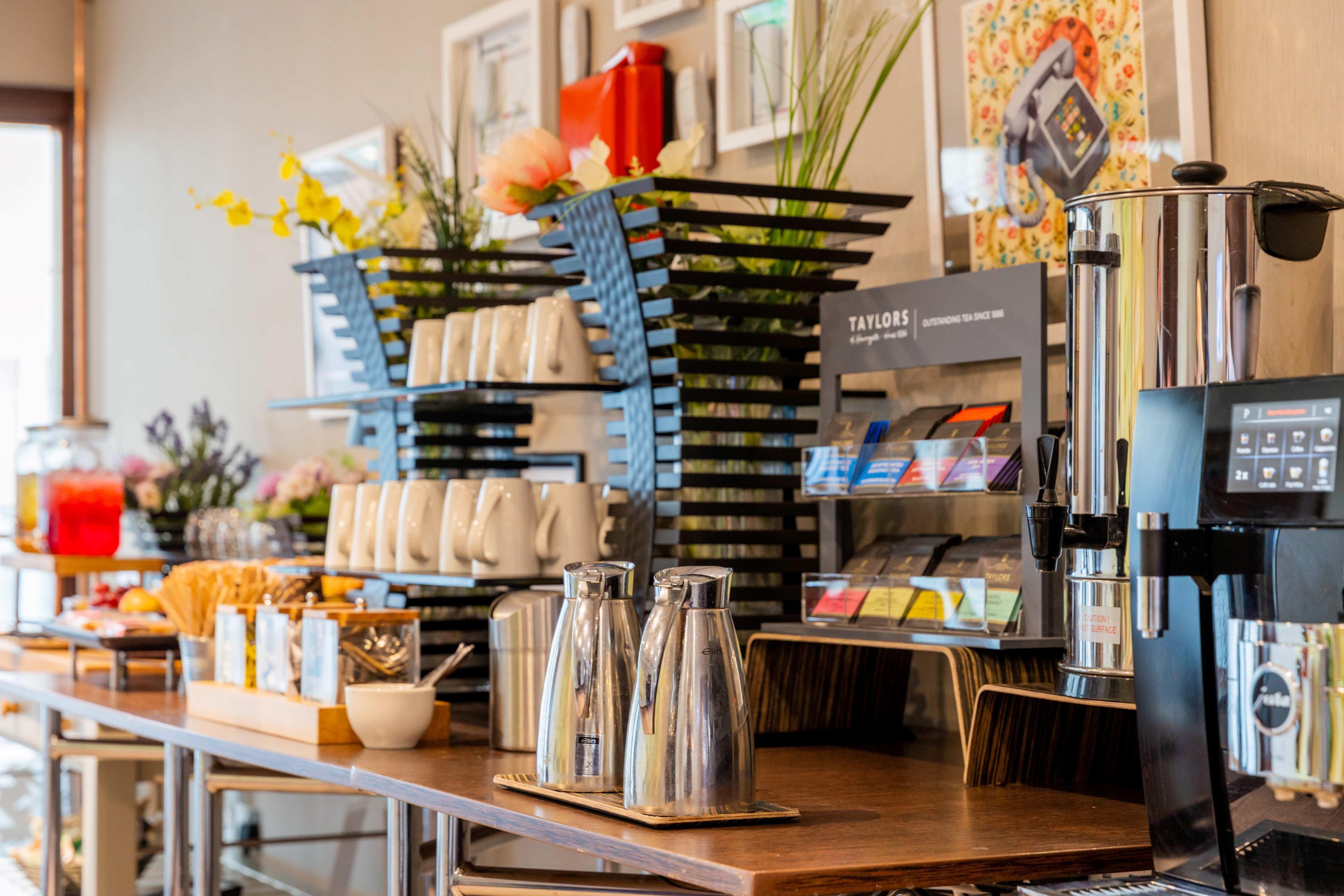A coffee shop counter with a coffee machine, a menu board, and various coffee cups and mugs.