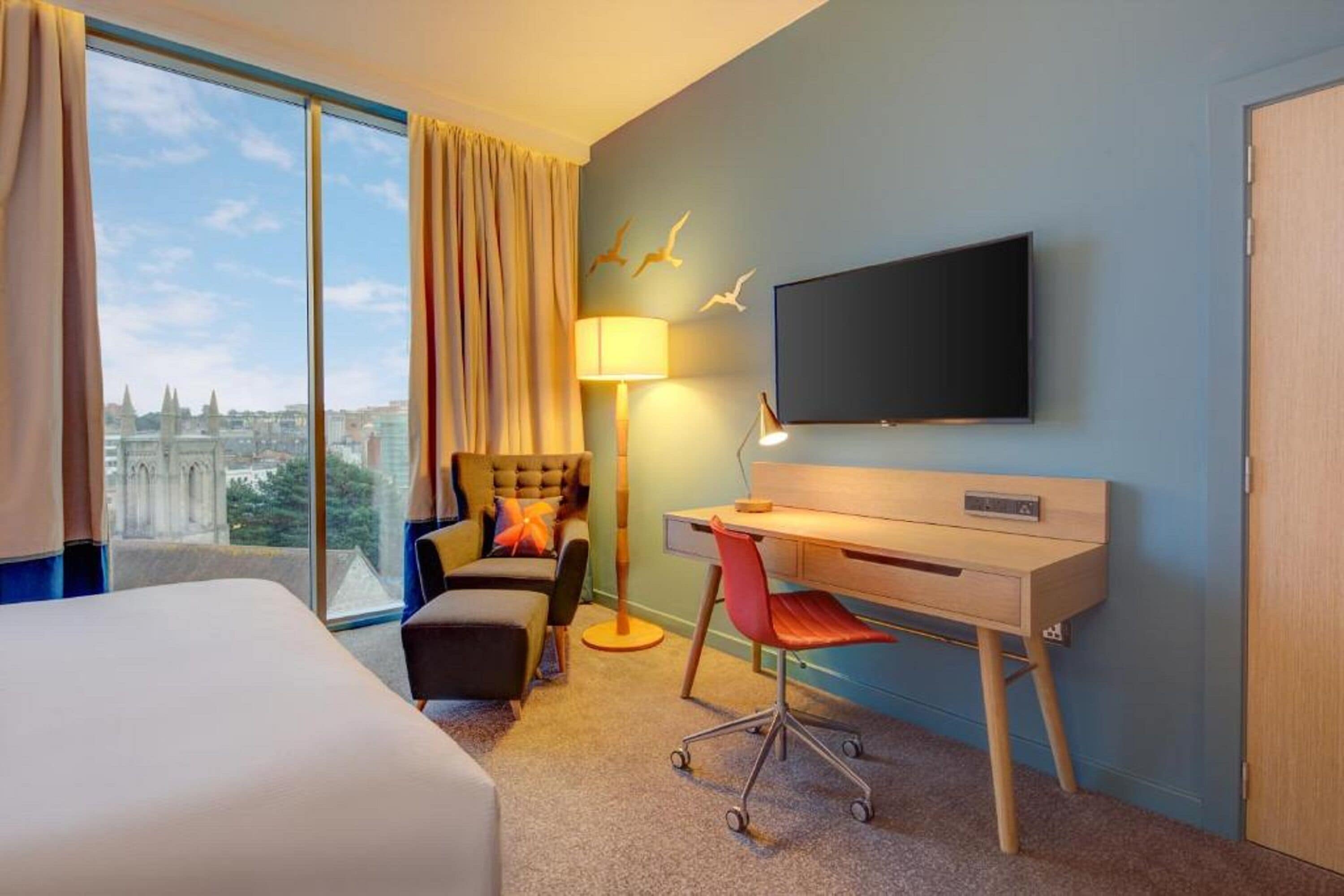 Habitación de hotel con una cama, un escritorio con silla, televisión y vistas a la ciudad.
