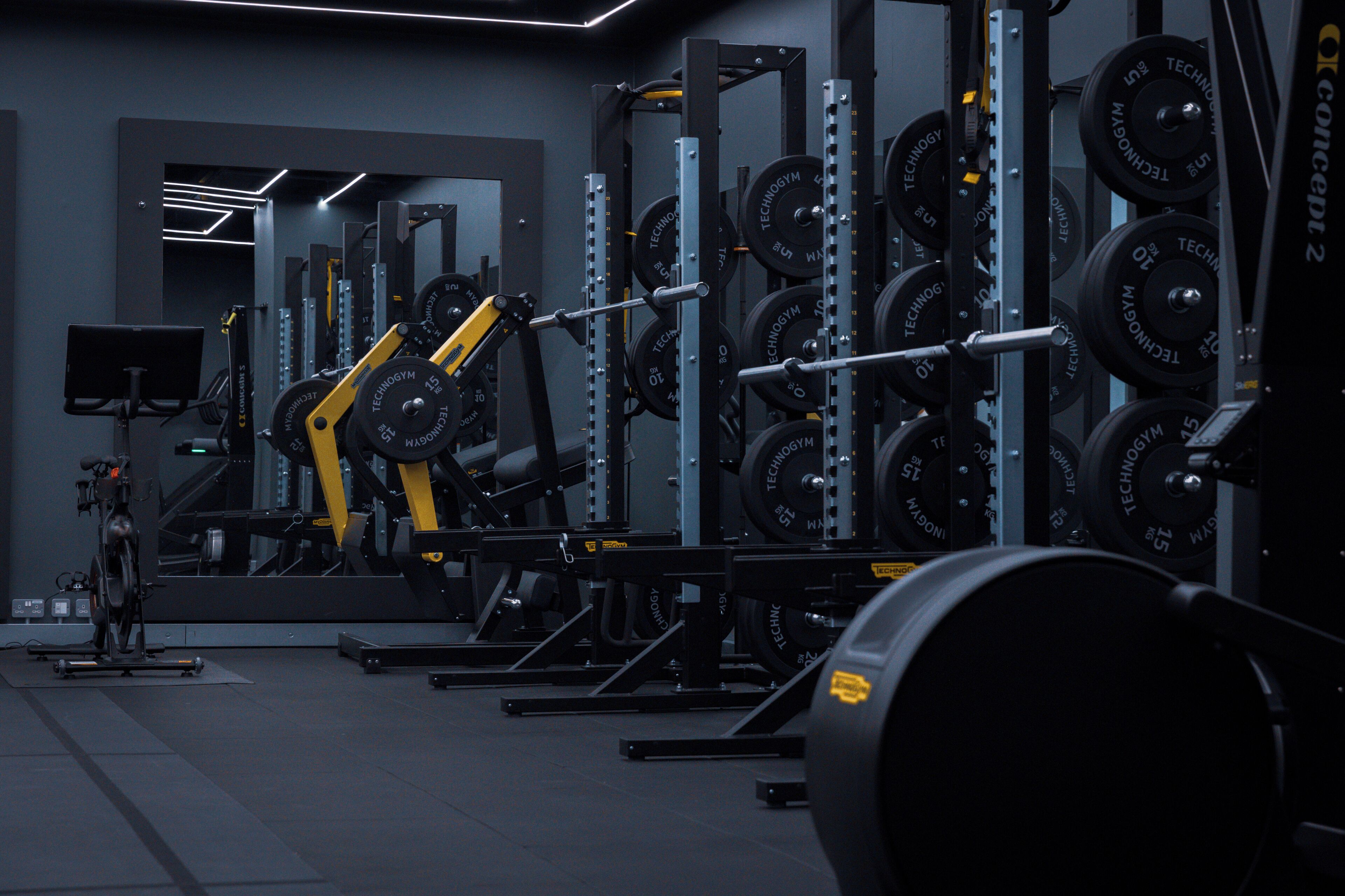 A gym with weightlifting equipment, including barbells and weight plates, arranged in rows.