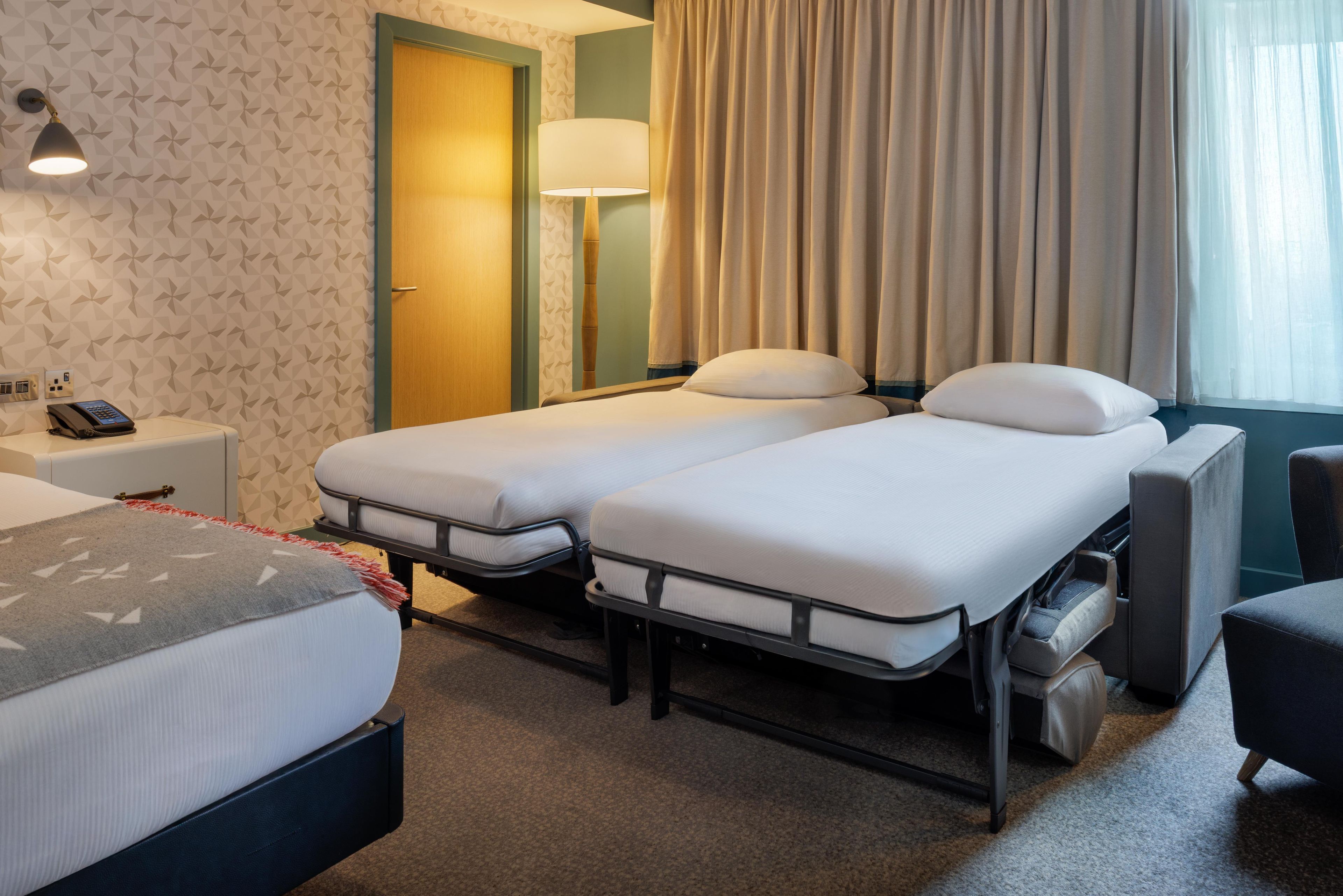 A hotel room with two beds, a desk, a lamp, and a window with curtains.