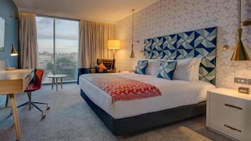 A hotel room with a large bed, a desk, a chair, and a view of the city.