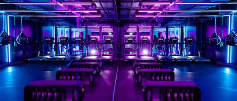 A gym with treadmills and punching bags, illuminated by purple and blue lighting.