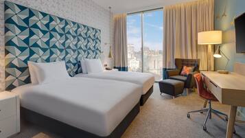A hotel room with a large bed, a desk, a chair, and a view of the city.