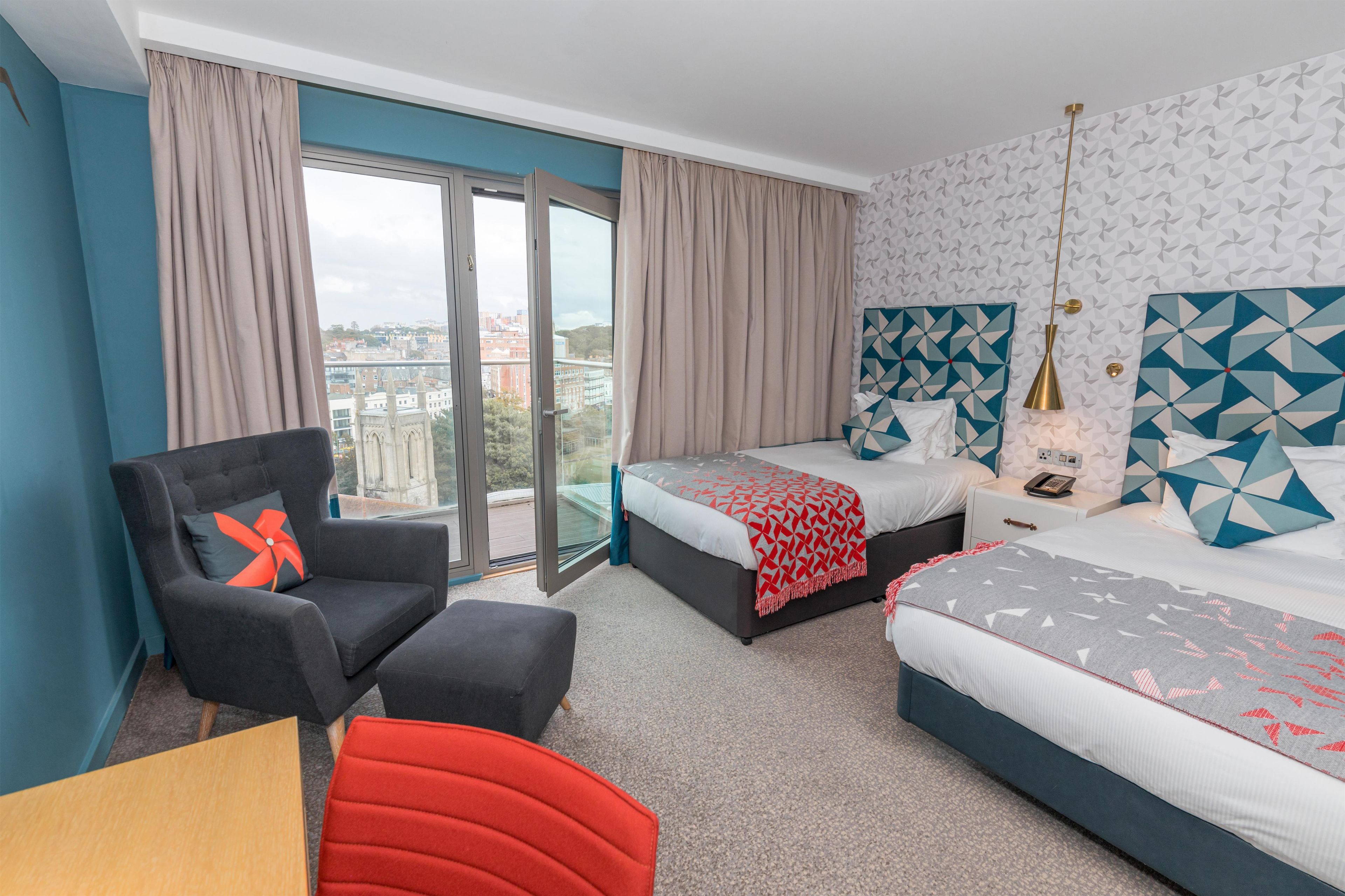 Habitación de hotel con cama, una silla, un escritorio y vista a la ciudad.
