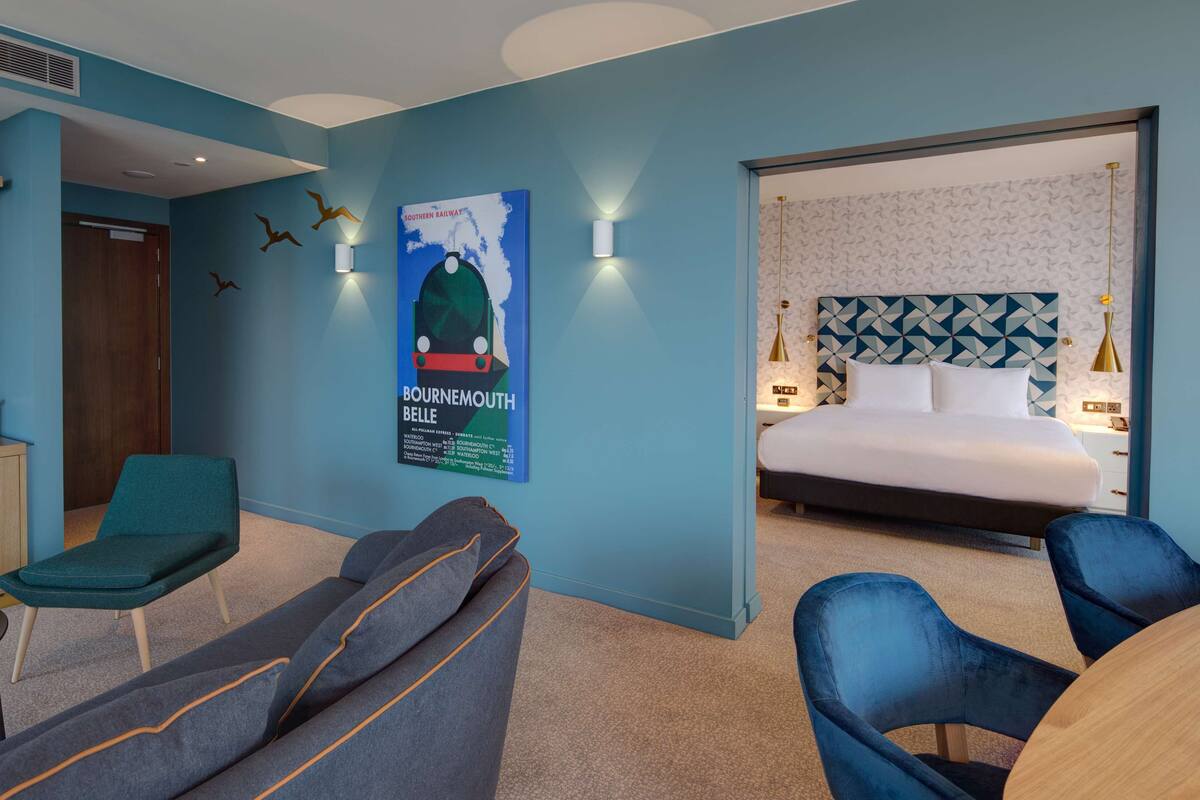A hotel room with a bed, a seating area with chairs, a poster on the wall, and a small table.