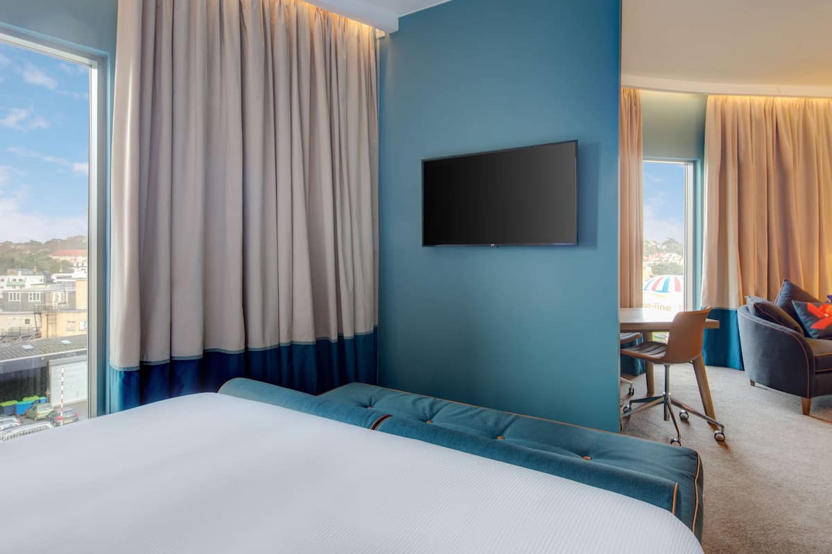 A hotel room with a large bed, a desk, a TV, and a view of the city.