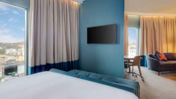 A hotel room with a large bed, a desk, a TV, and a view of the city.