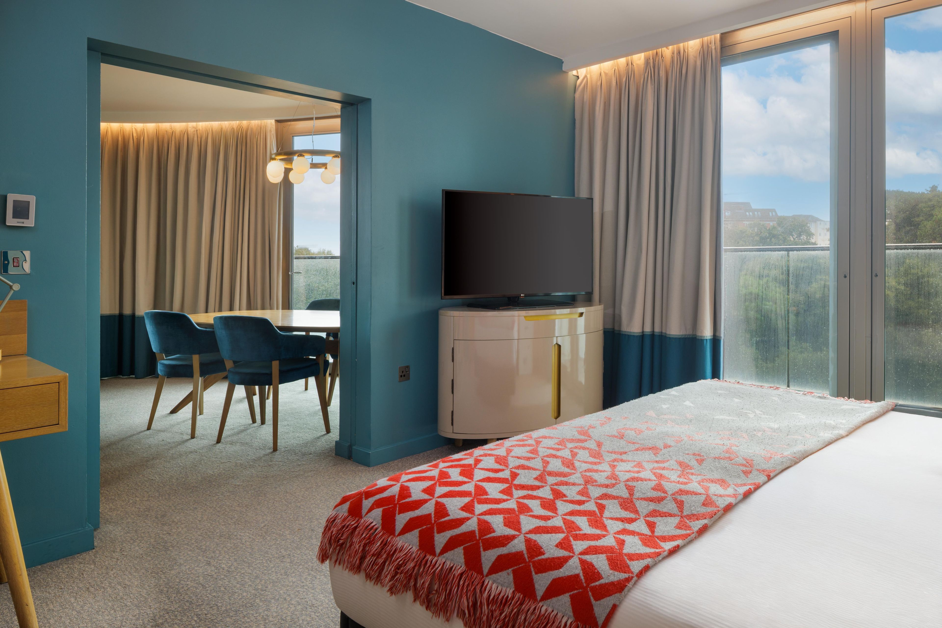 A hotel room with a bed, a desk with chairs, a television, and a view of the outdoors.