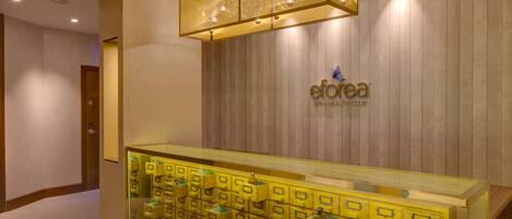 A hotel reception area with a wooden wall, a glass display case with yellow storage boxes, and a hanging light fixture.