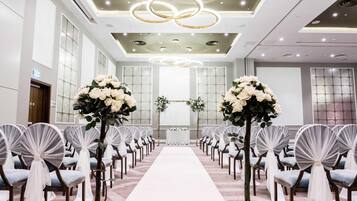 A hotel chapel with a white aisle, pews with white and blue cushions, and a floral arrangement at the altar.