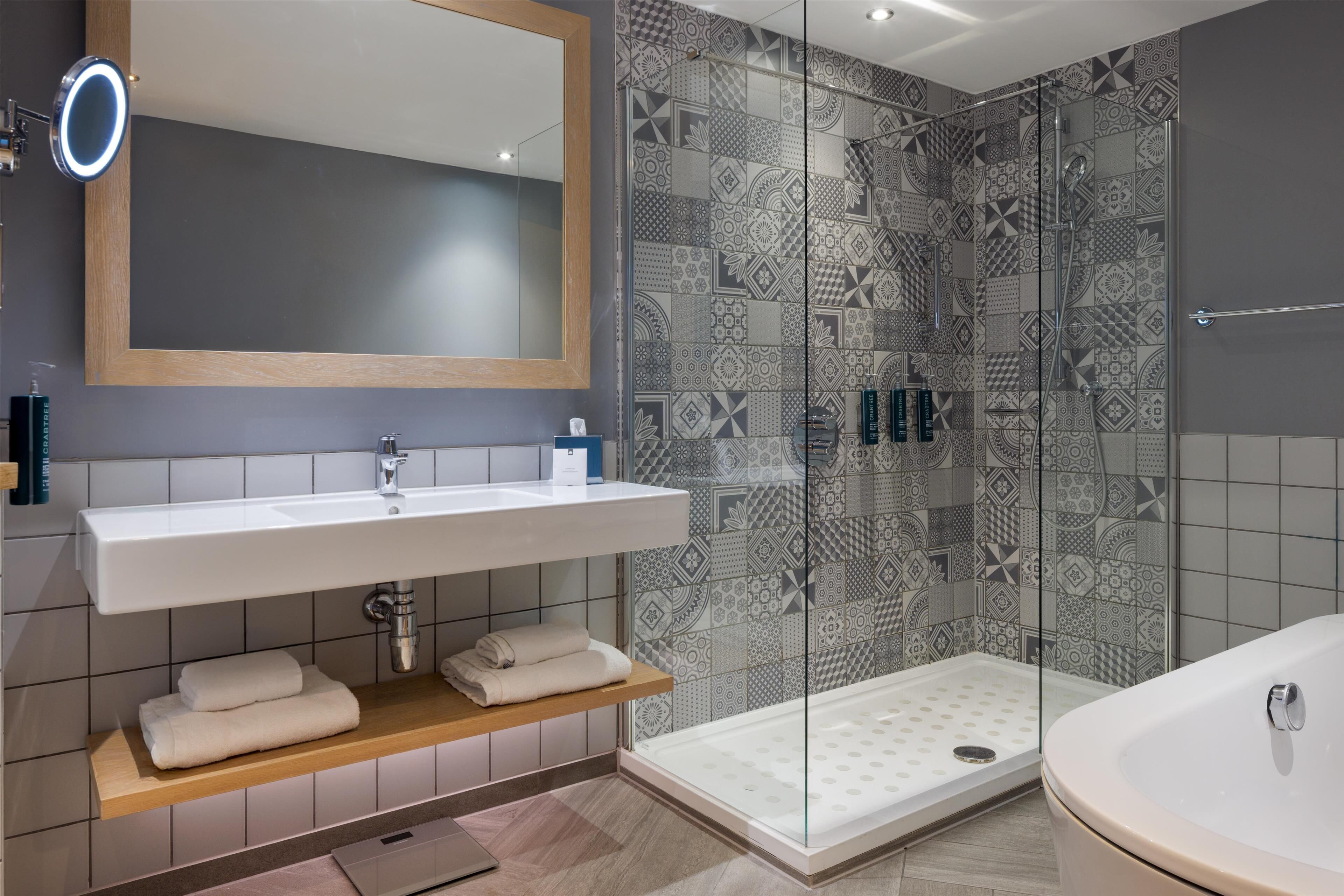 A modern bathroom with a large mirror, white sink, and a glass-enclosed shower area.