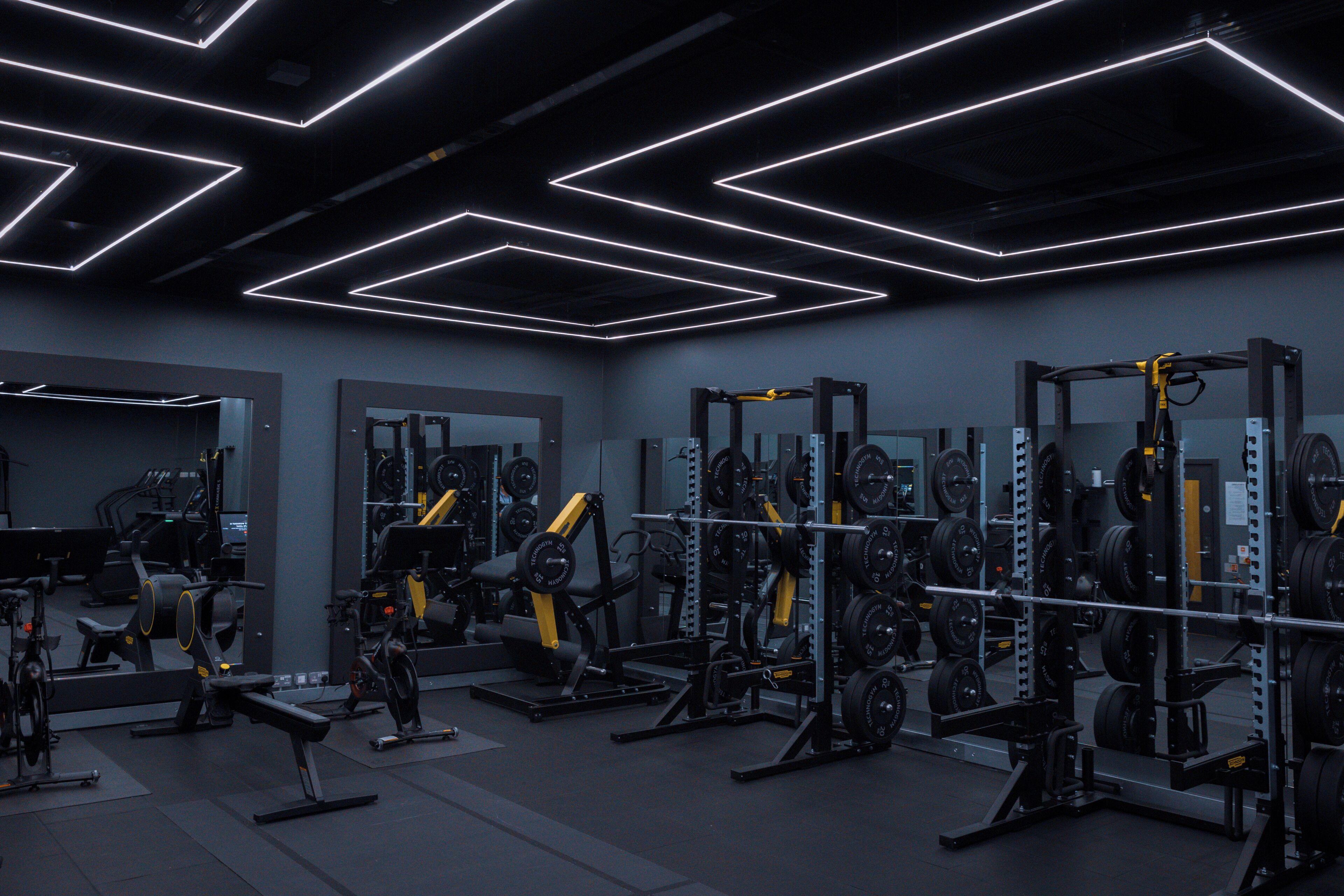A gym with various weightlifting equipment, mirrors, and a modern geometric ceiling design.