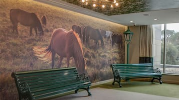 A room with a mural of horses, two green benches, and a ceiling with a light fixture.