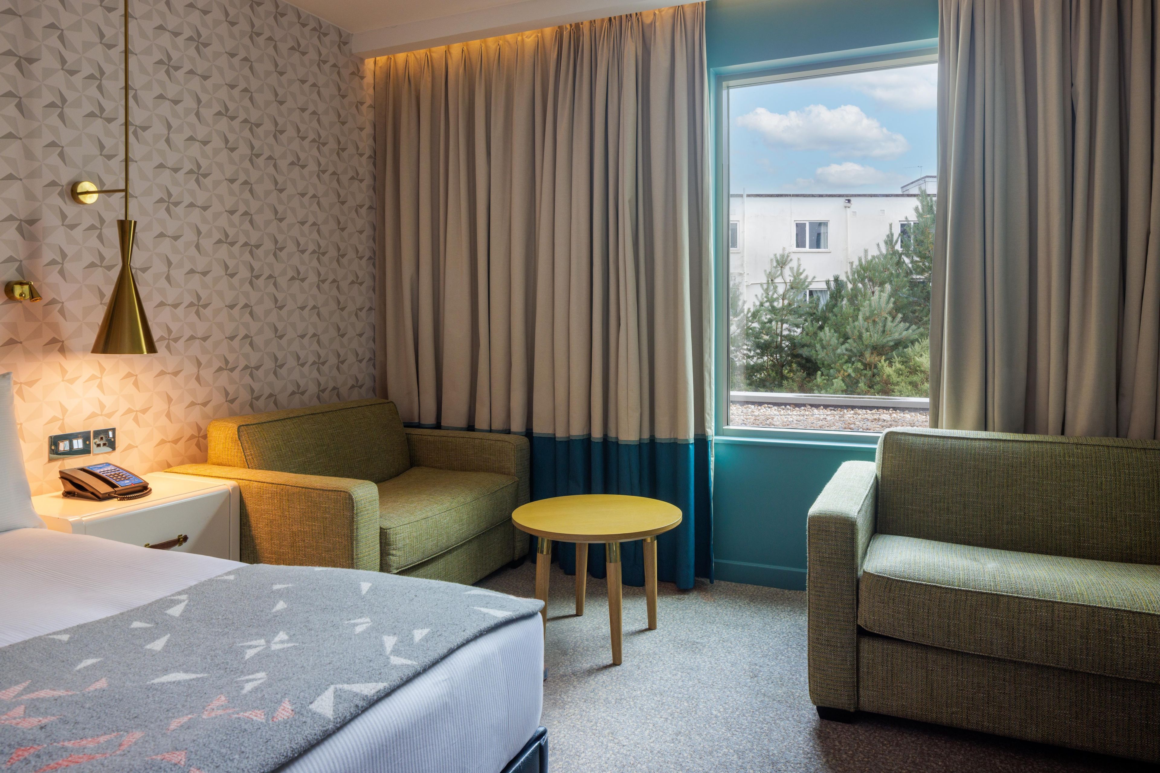 A hotel room with a bed, two armchairs, a small table, and a window with curtains.