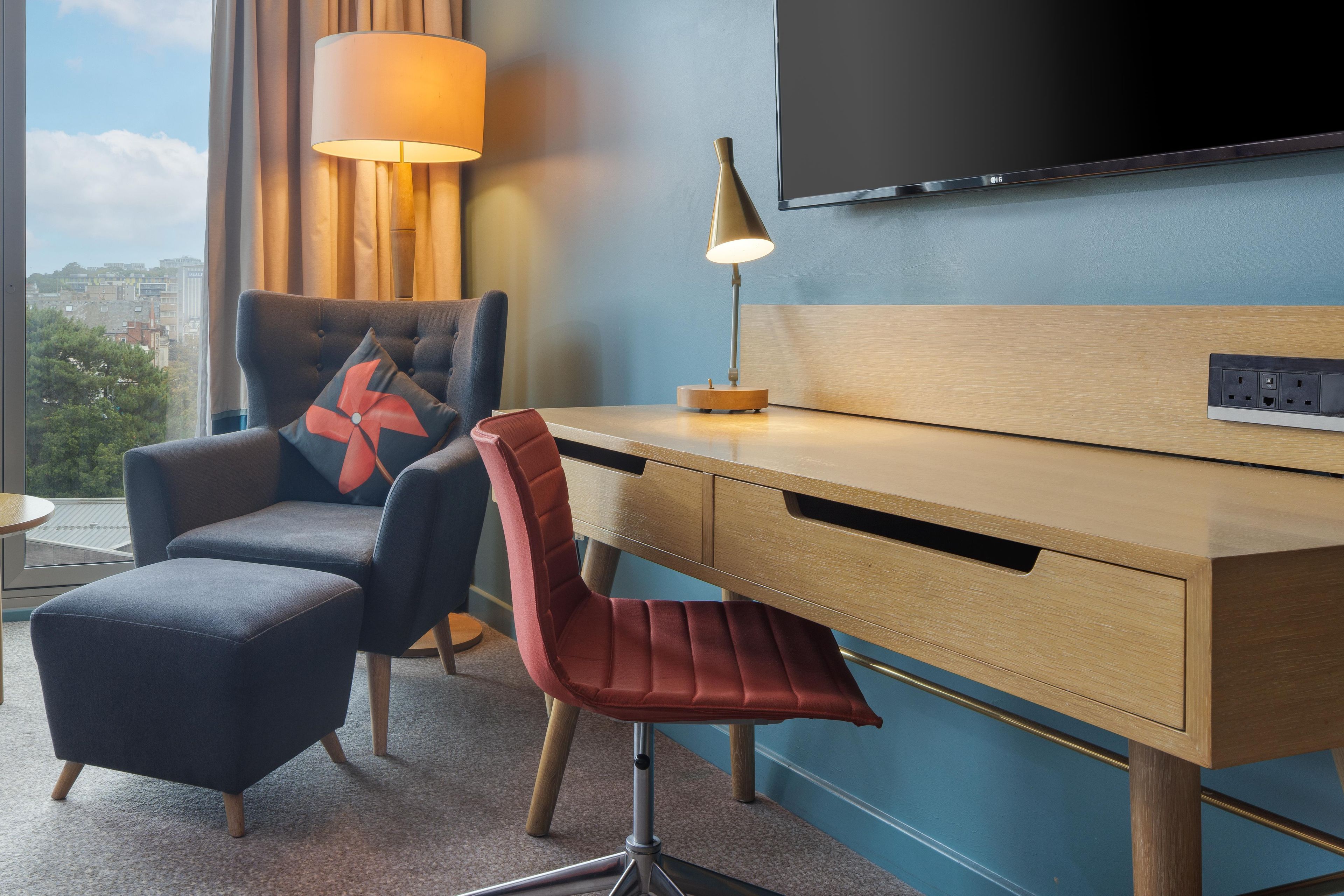 Een hotelkamer met een bureau, stoel, televisie, lamp en uitzicht op de stad.