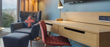 Een hotelkamer met een bureau, stoel, televisie, lamp en uitzicht op de stad.