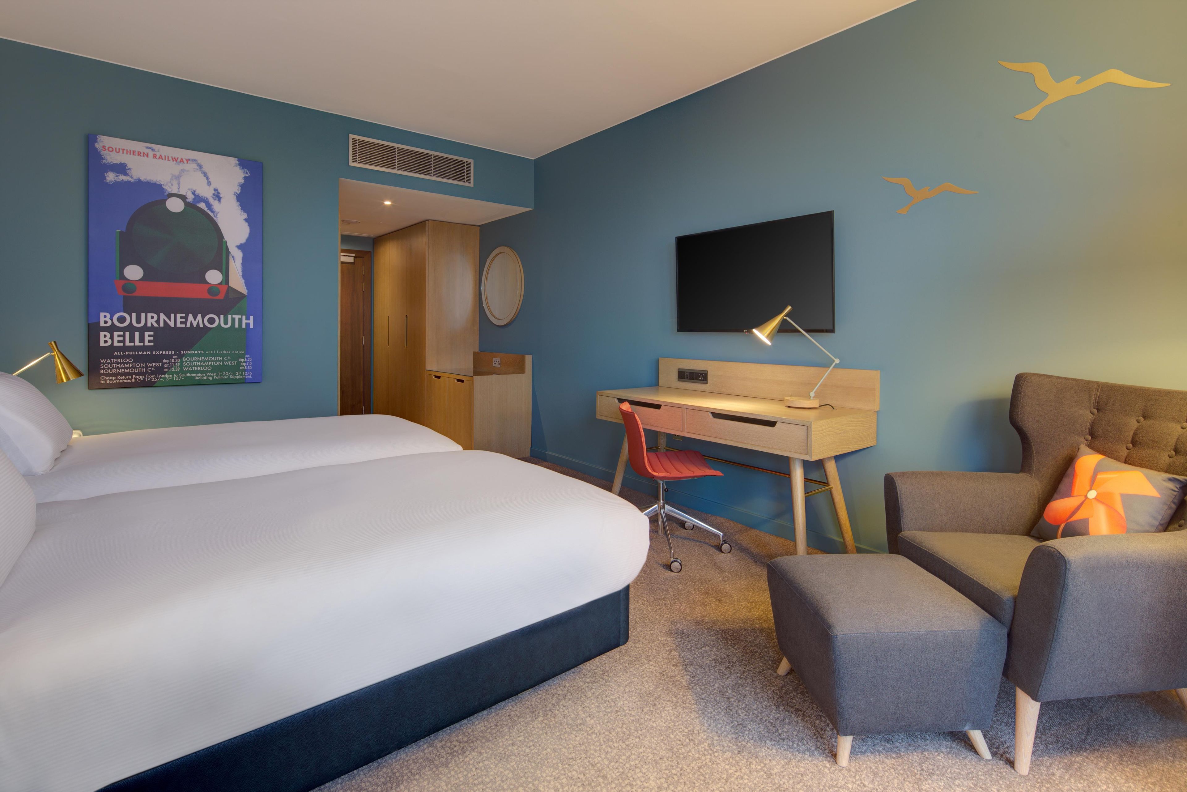 Ein Hotelzimmer mit Bett, Schreibtisch, Stuhl, Fernseher und einem Bild an der Wand.