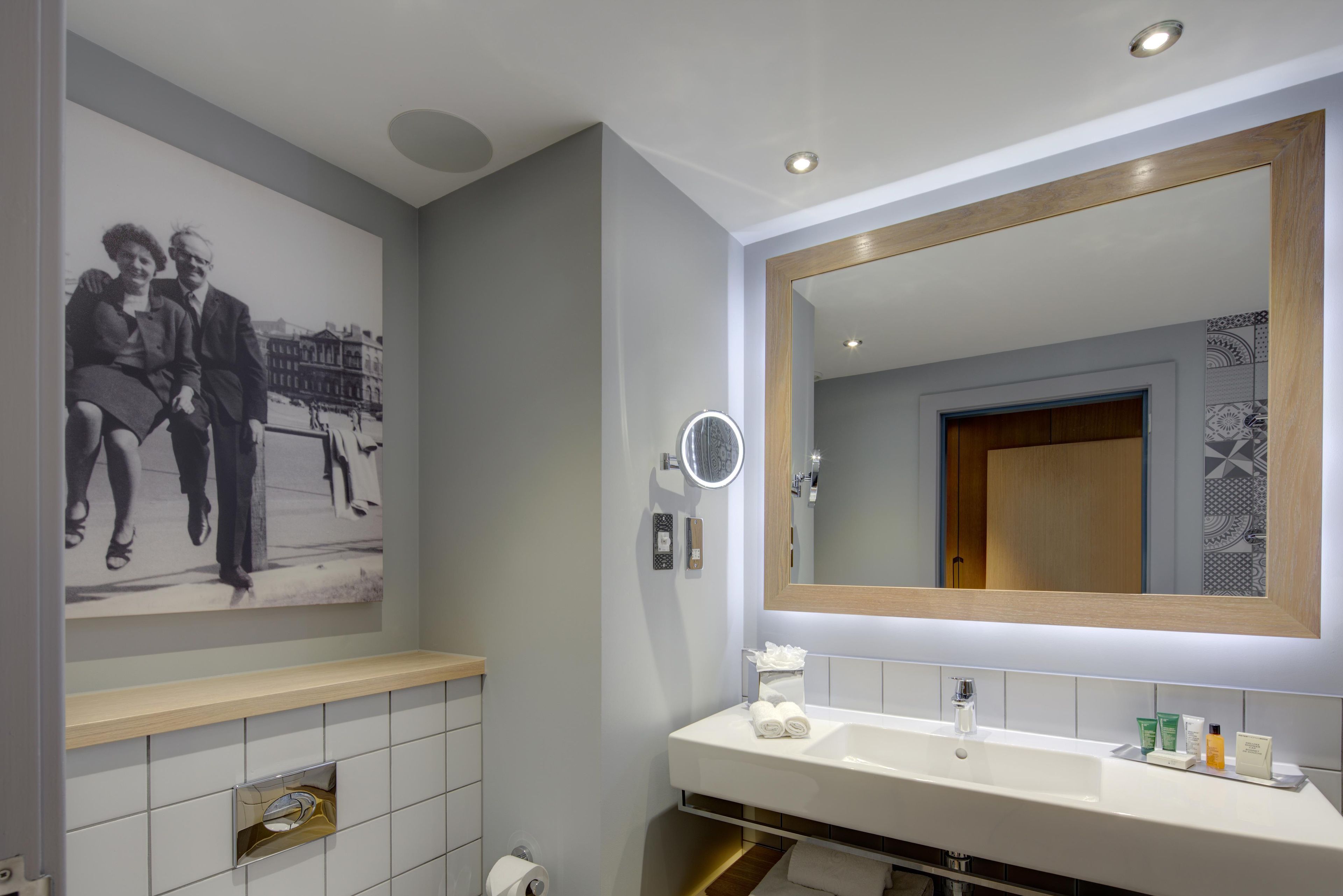 A modern bathroom with a large mirror, a sink with toiletries, and a wall-mounted toilet paper holder.