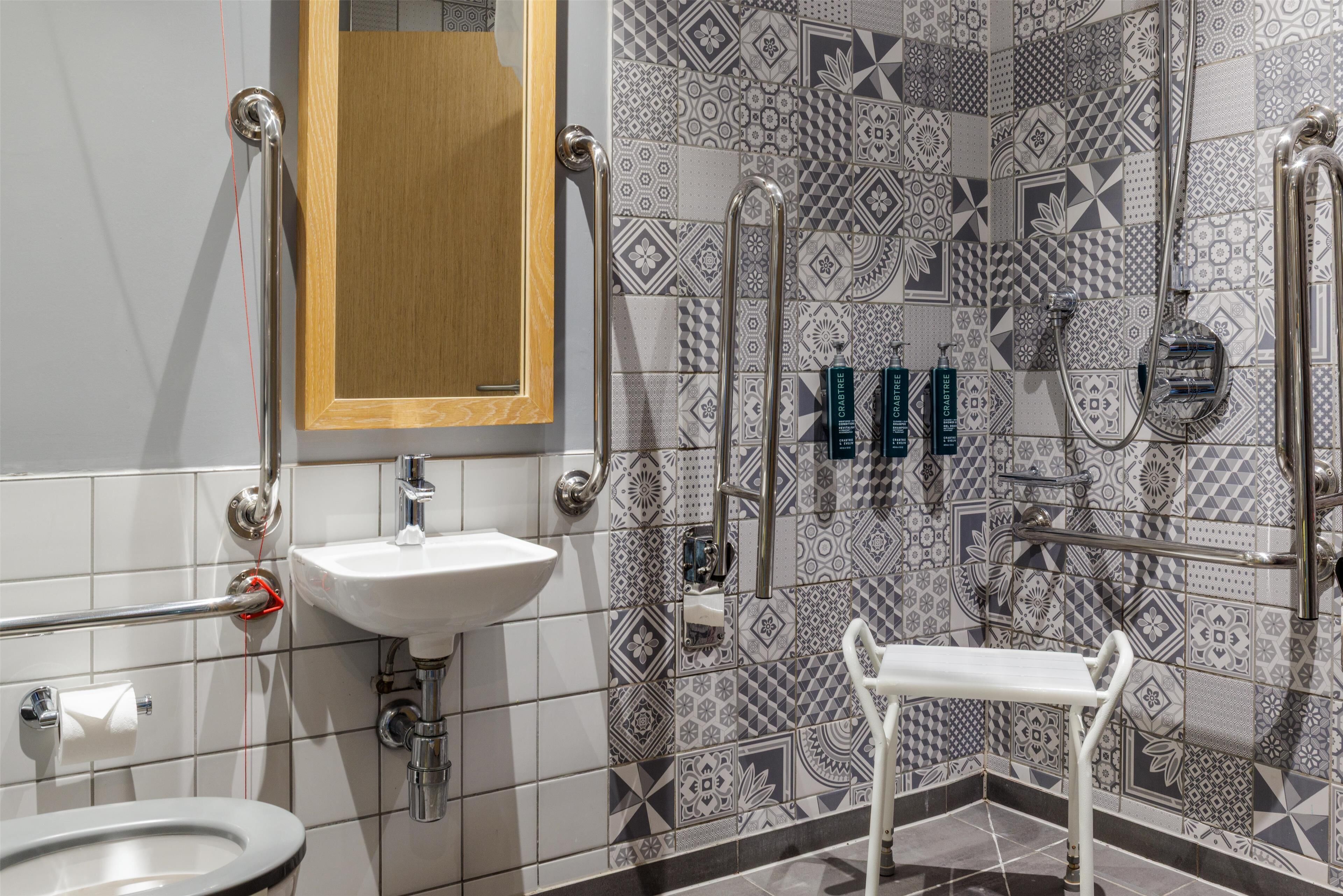 A bathroom with a white sink, a mirror, a toilet, a shower area, and a grab bar.
