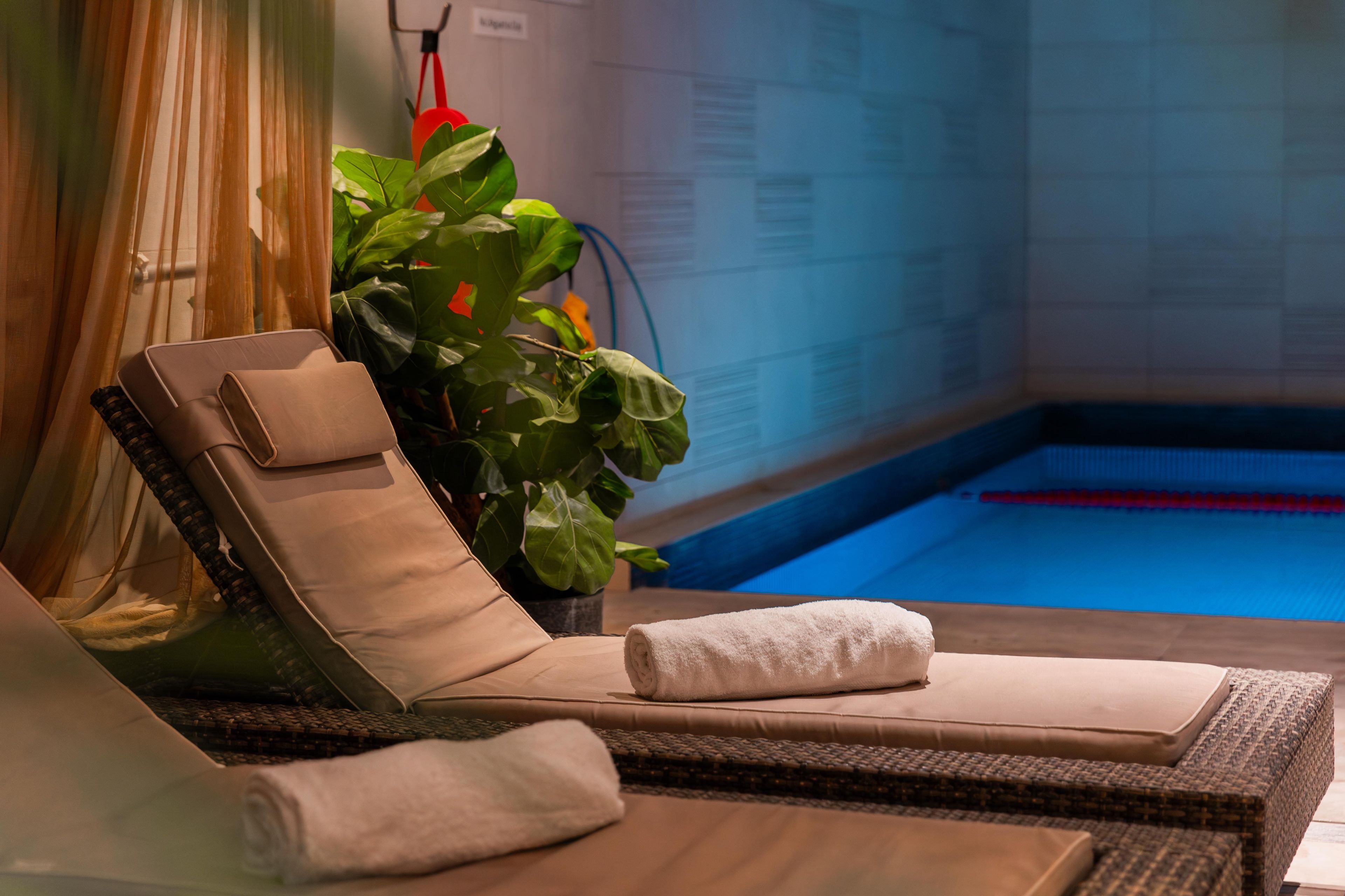 Una silla de salón con una toalla, una planta en maceta y una piscina al fondo.