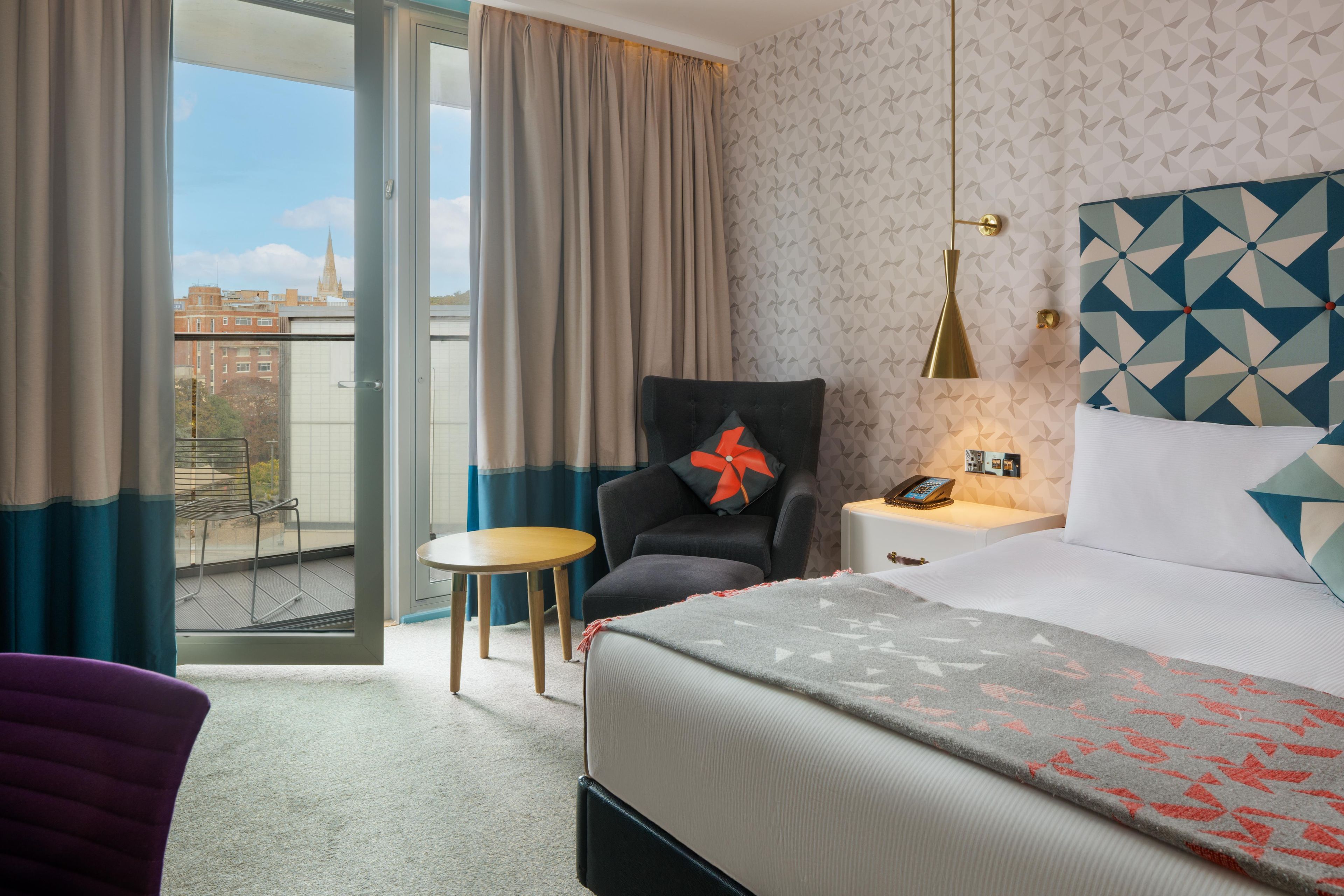 Ein Hotelzimmer mit Bett, Stuhl, kleinem Tisch und Blick auf die Stadt durch das Fenster.