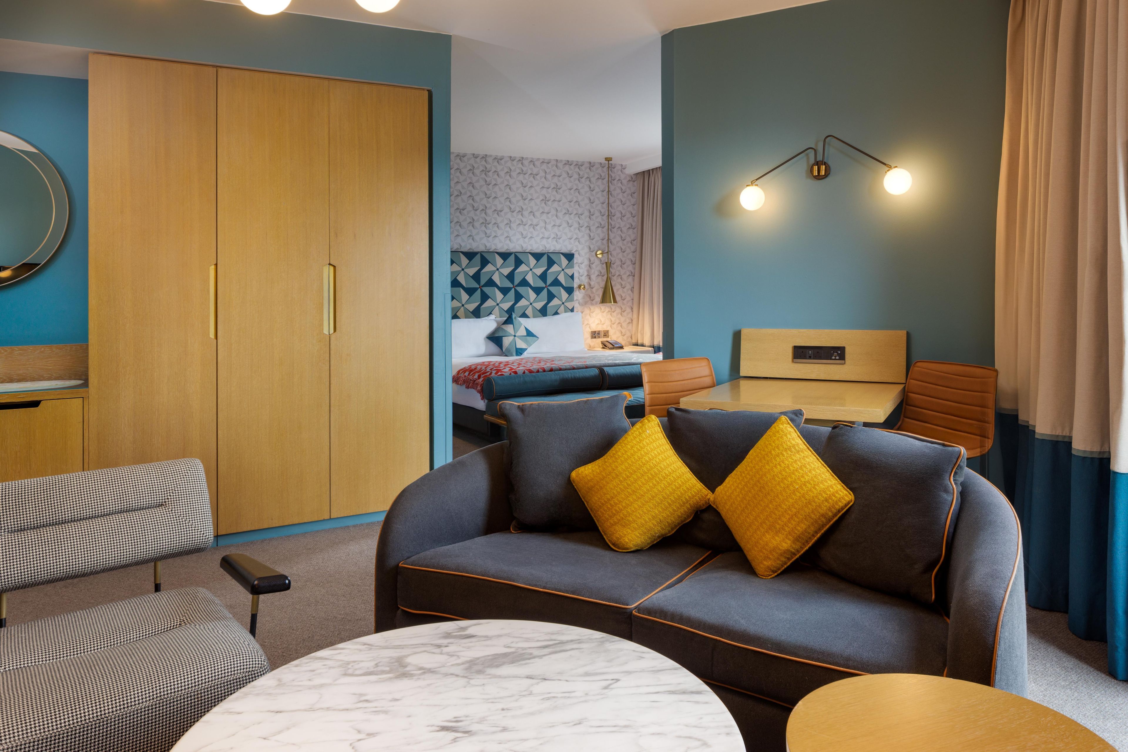 A modern living room with a sofa, a coffee table, and a bed with a geometric-patterned headboard.