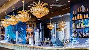 Zona de bar con varios candelabros, una barra con utensilios y estantes con botellas.