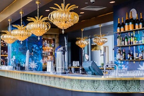 A bar area with multiple chandeliers, a counter with bar tools, and shelves with bottles. - Hilton Bournemouth (Bournemouth)