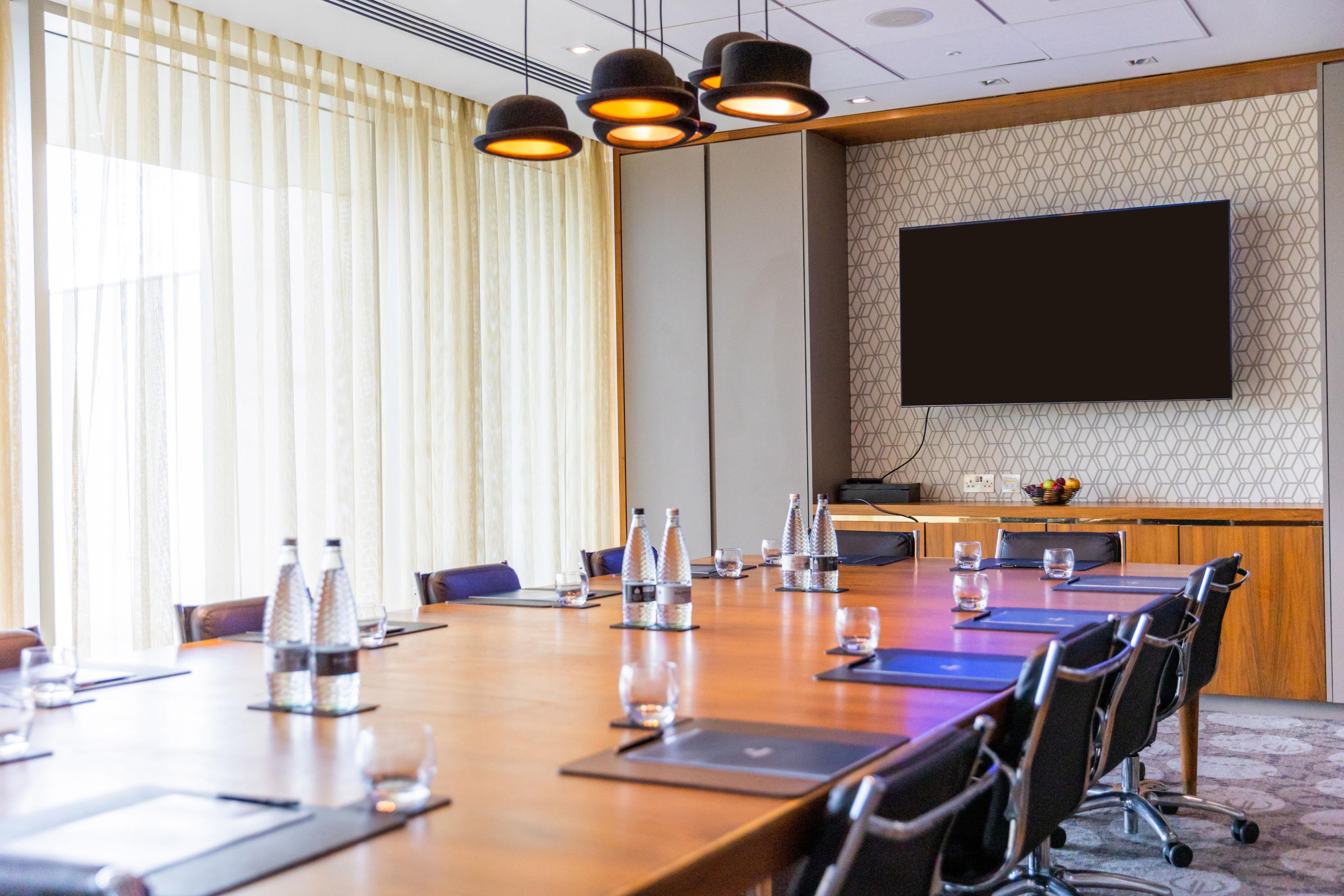 A conference room with a long table, chairs, water bottles, glasses, a projector screen, and a patterned wall.