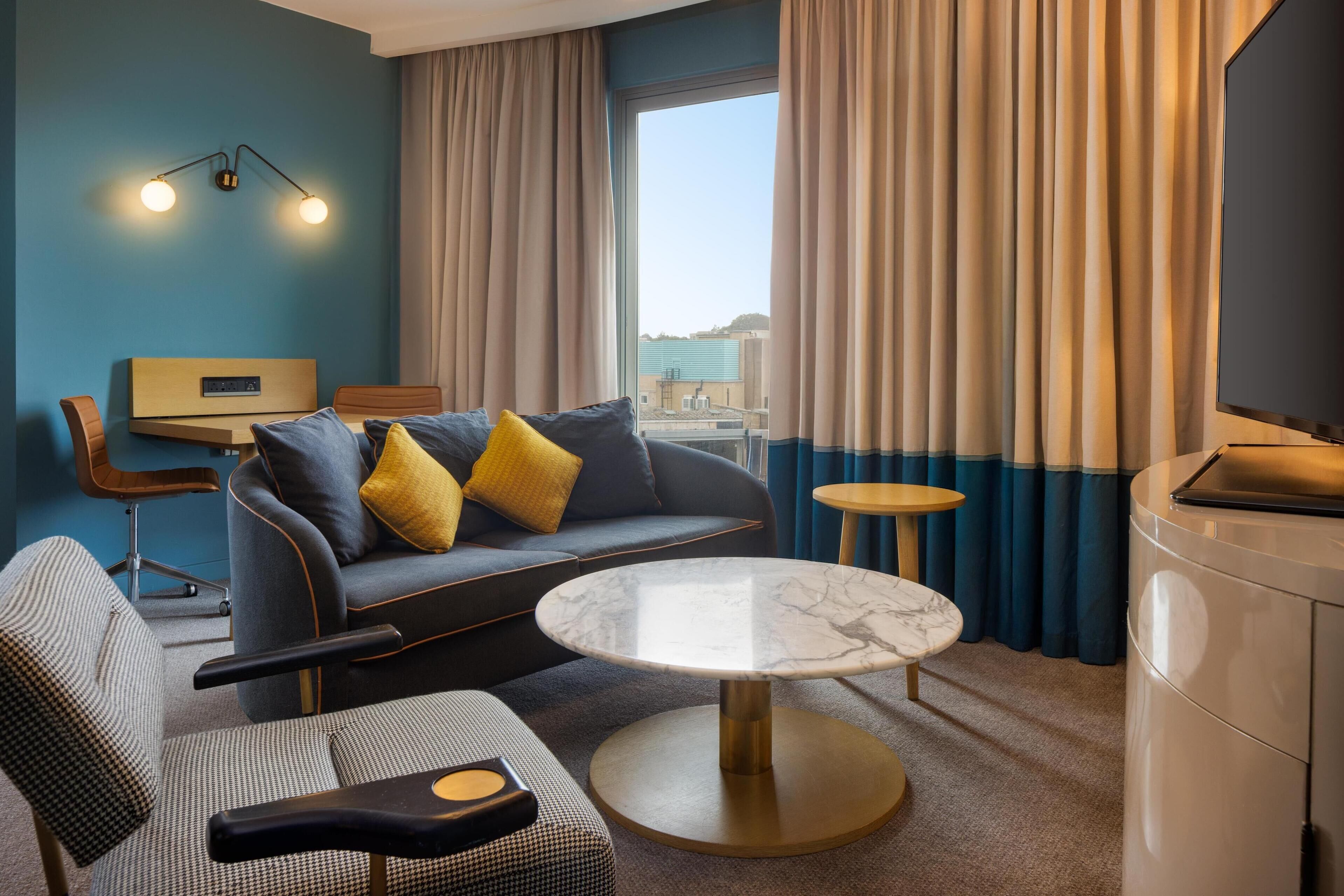 Een moderne hotelkamer met een bank, fauteuil en een ronde marmeren tafel.