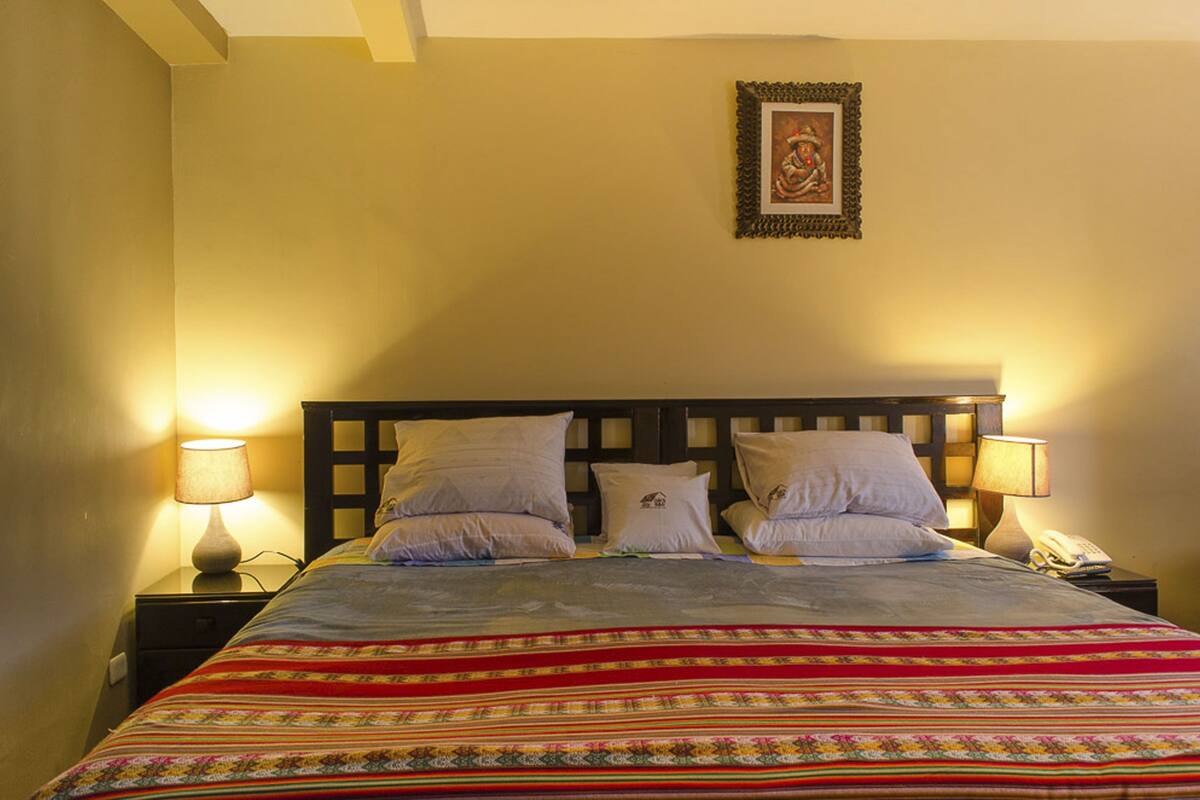 A neatly made bed with a colorful blanket, two bedside lamps, and a framed picture on the wall.