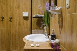 A bathroom with a wooden vanity, a white sink, a mirror, and a shelf with toiletries. - Cusco Bed and Breakfast (Cusco)