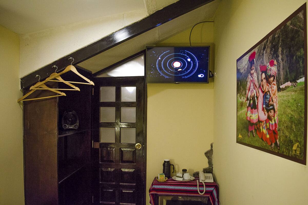 A room with a wooden door, a wall-mounted TV displaying a space-themed image, and a painting of people in traditional attire.