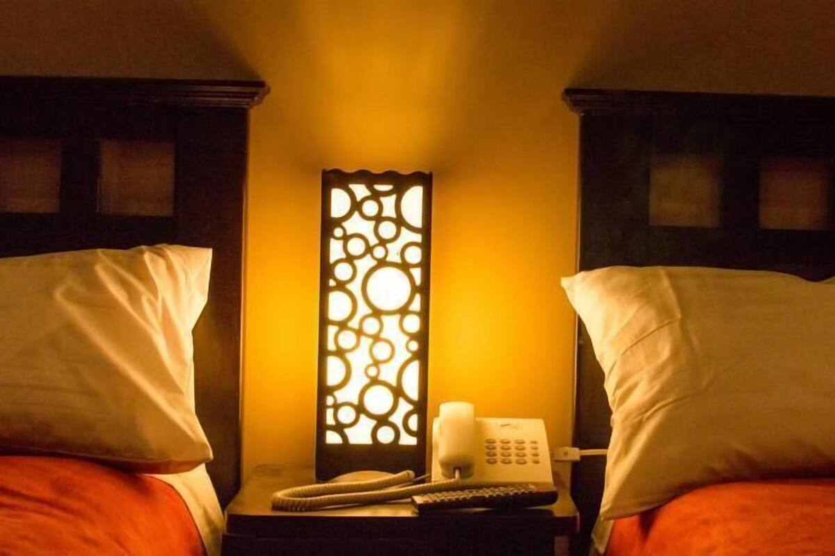 A hotel room with two beds, a nightstand with a telephone and a remote control, and a decorative wall panel.