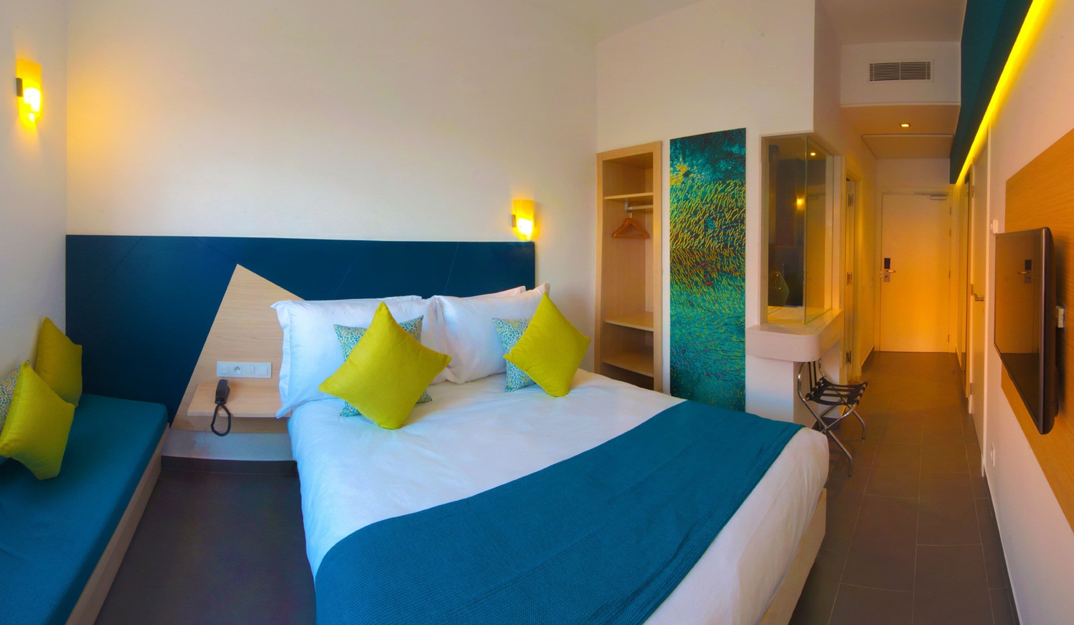 A hotel room with a large bed, a bedside table, a mirror, and a wardrobe.