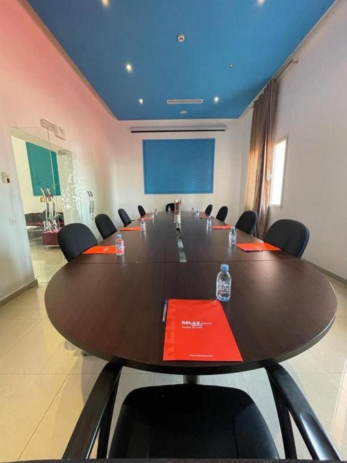 Un salón de conferencias con una larga mesa, sillas negras y manteles individuales rojos.