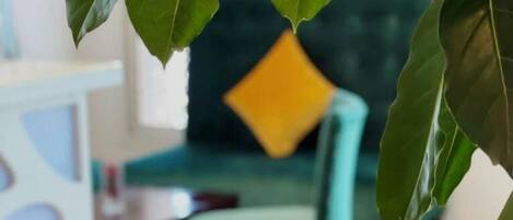 A room with a green sofa and a yellow pillow, a white table, and a plant with large green leaves.