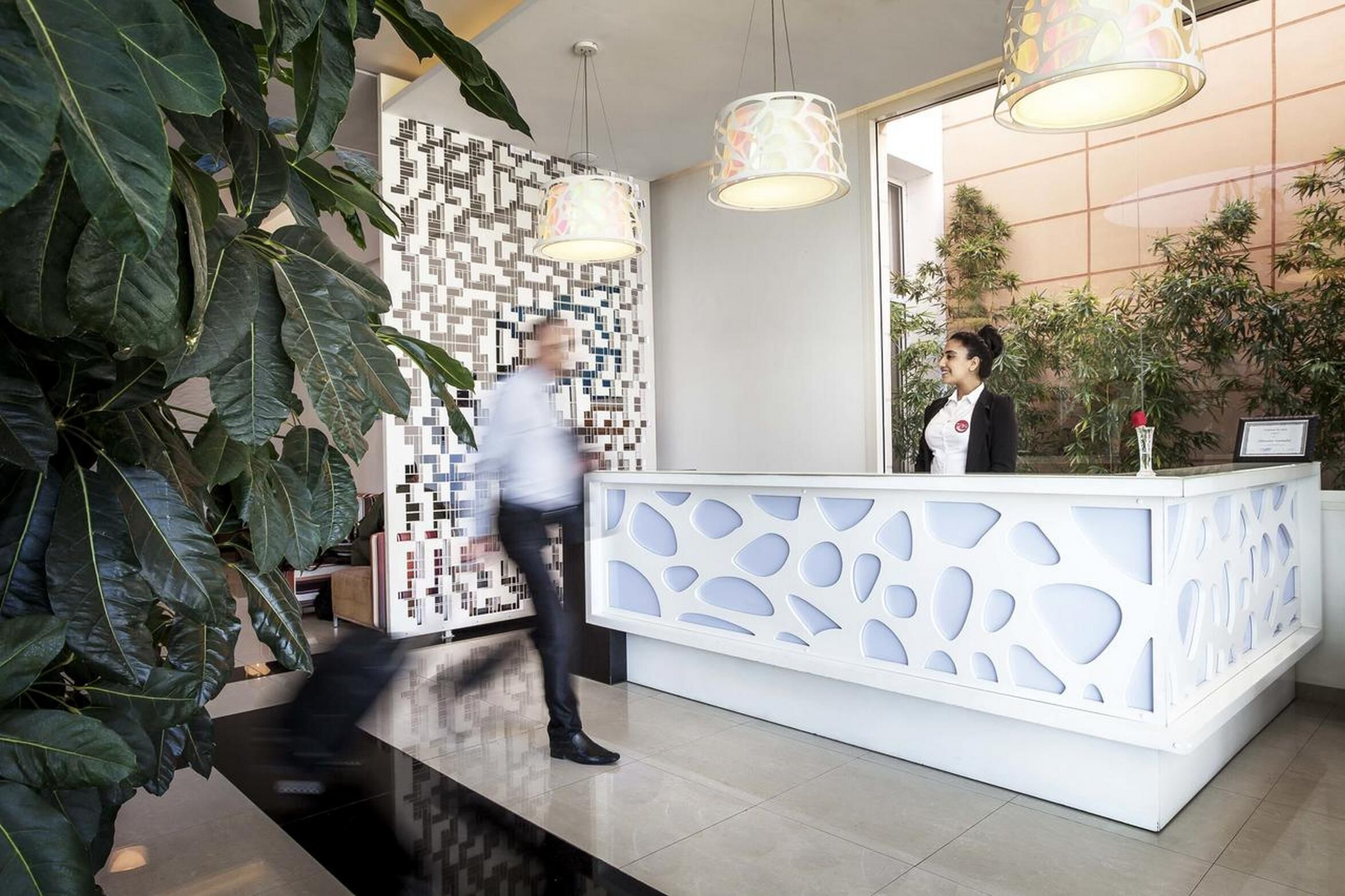 Un mostrador de recepción de diseño moderno, plantas en macetas grandes y decoración mural con patrones.