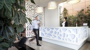 Un mostrador de recepción de diseño moderno, plantas en macetas grandes y decoración mural con patrones.