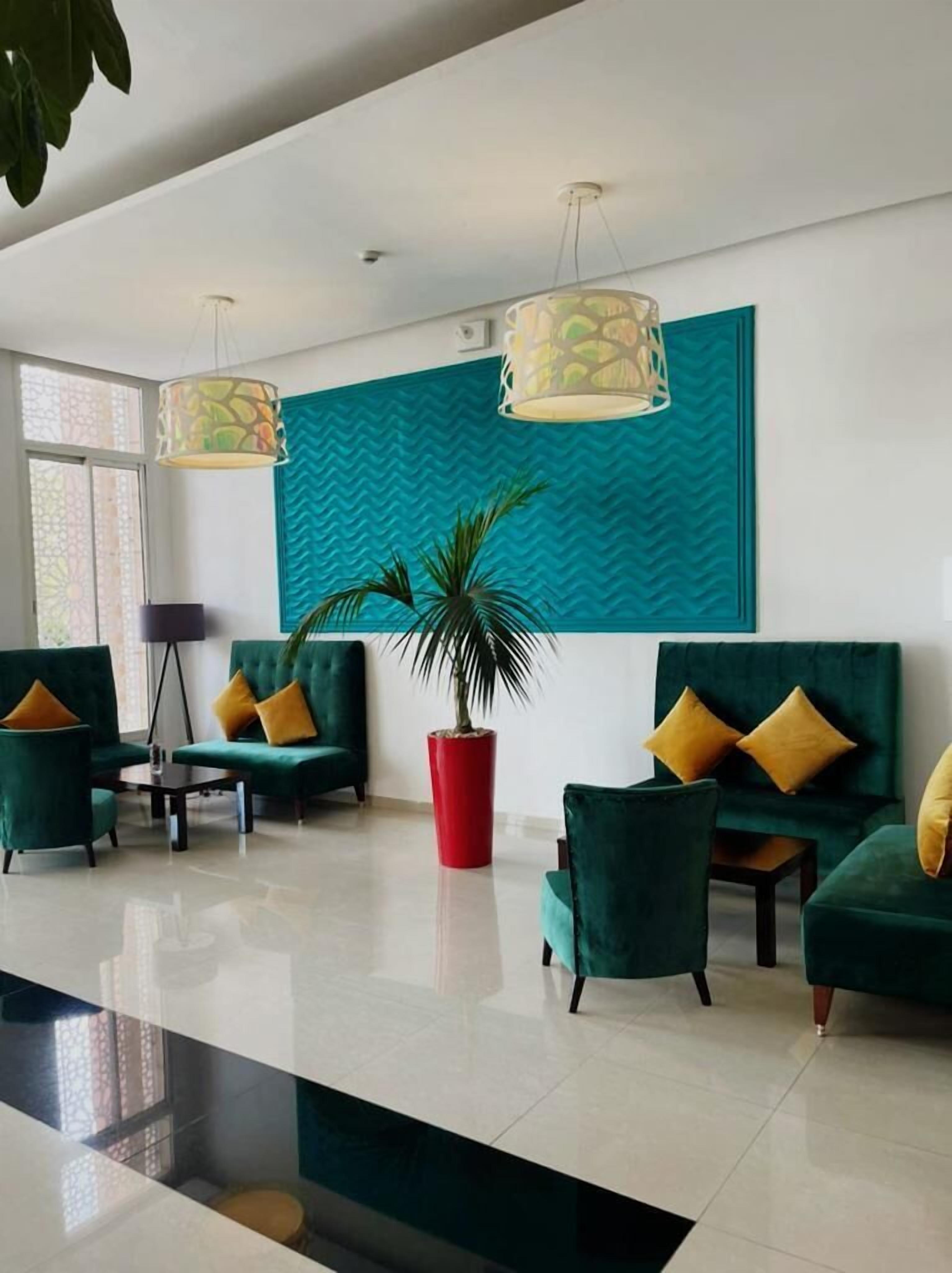 A modern living room with teal and green sofas, a red planter, and pendant lights.