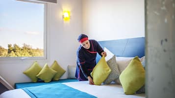 Cama com cabeceira azul, almofadas verdes e uma pessoa ajeitando um travesseiro.