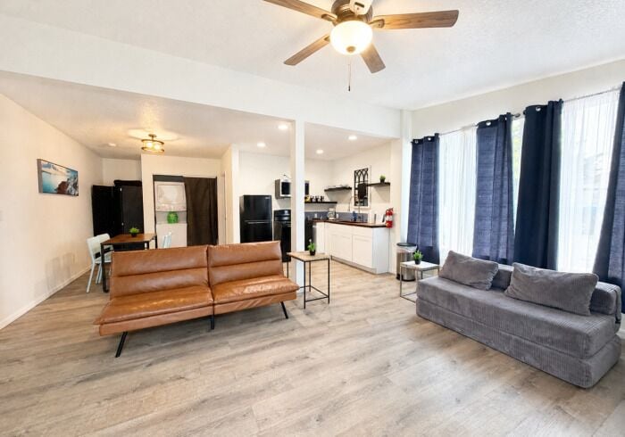 A modern living room with a sofa and a couch, a ceiling fan, and a kitchen area in the background.