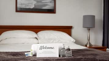 Een hotelkamer met een bed, een welkomstbord, een bedlamp en een ingelijst schilderij aan de muur.