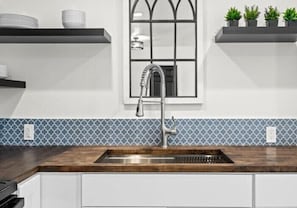 A kitchen with a wooden countertop, a stainless steel sink, and a window with a black frame. - Travel Inn of Titusville (Titusville)